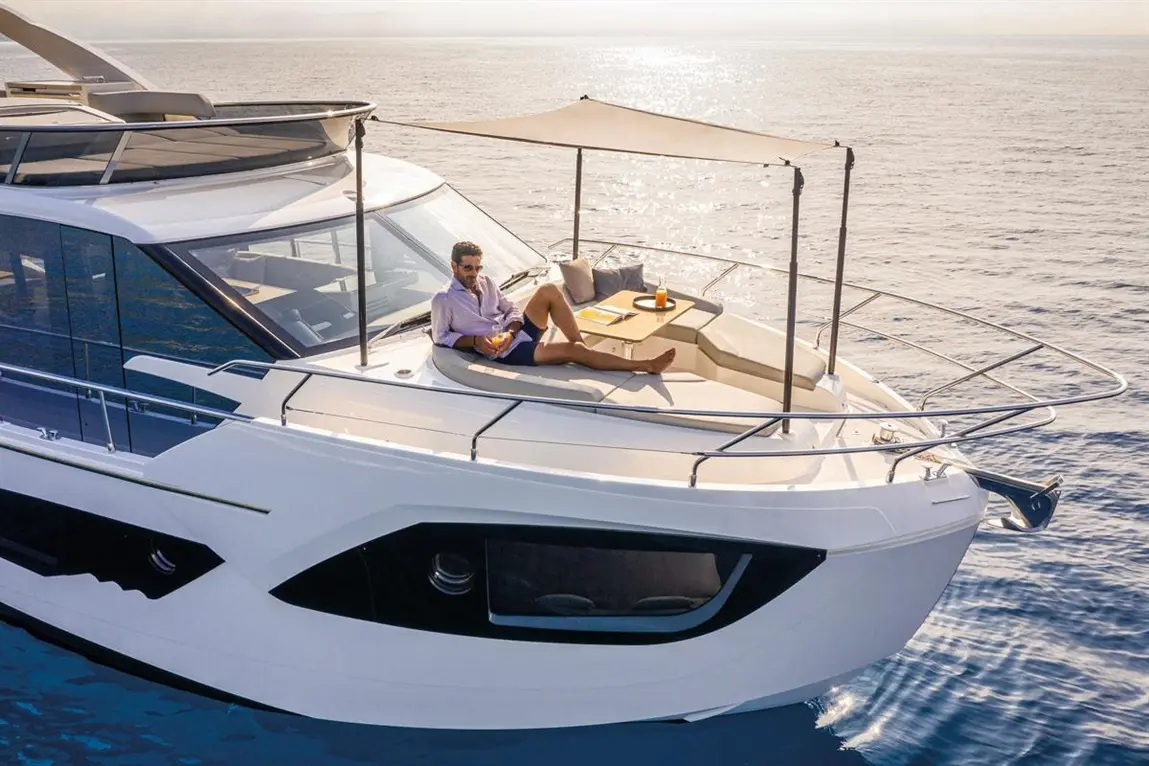 Man relaxing on a luxury yacht's bow, enjoying a drink with a notebook on a sunlit sea, surrounded by calm waters.